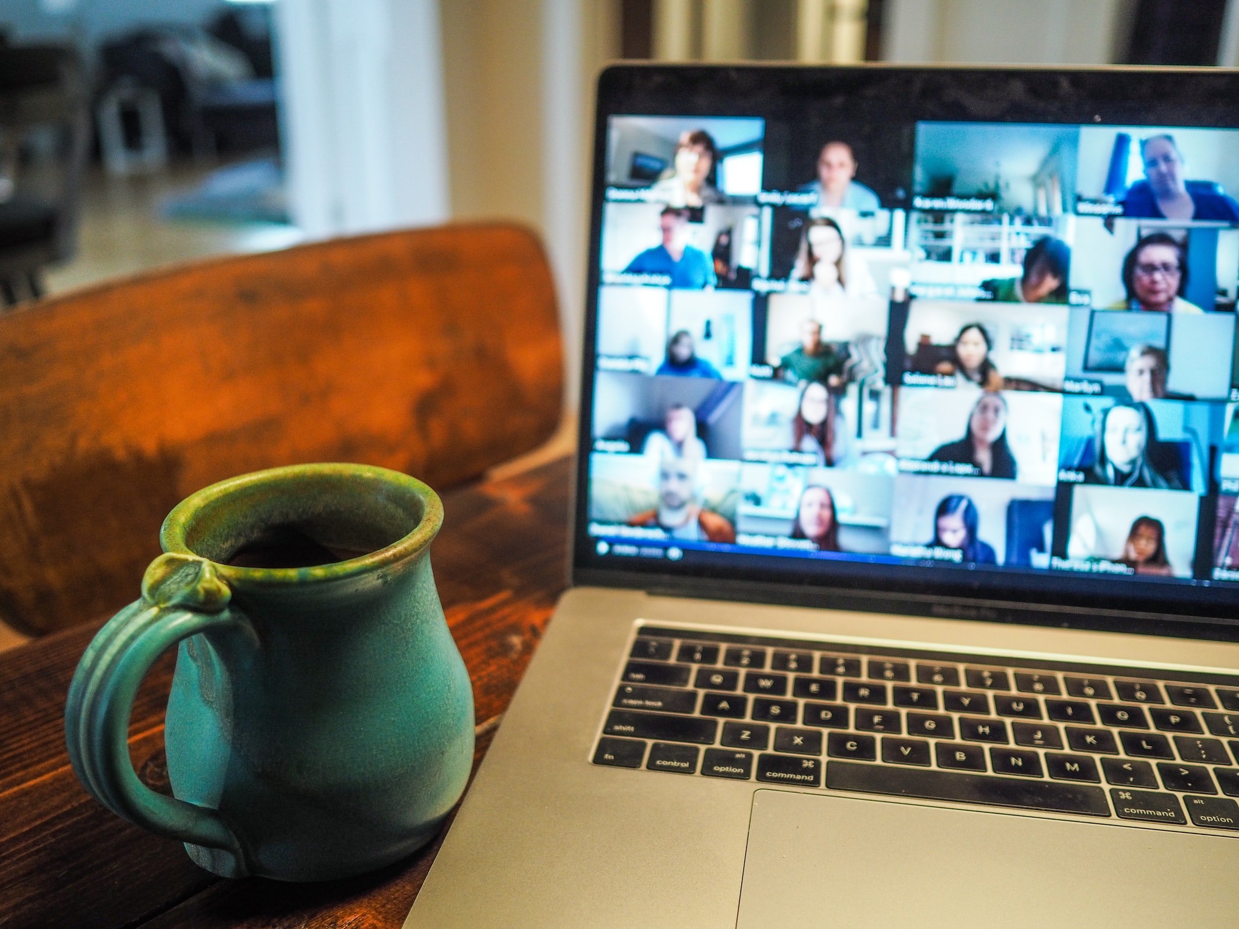 A coffee mug placed next to a laptop. Multiple participants of an online forum are displayed on the laptop screen.